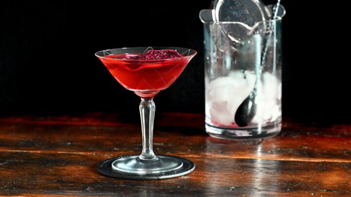 red Stranger Things Drink with dried dragonfruit chip garnish in cocktail coupe on wooden table with black background